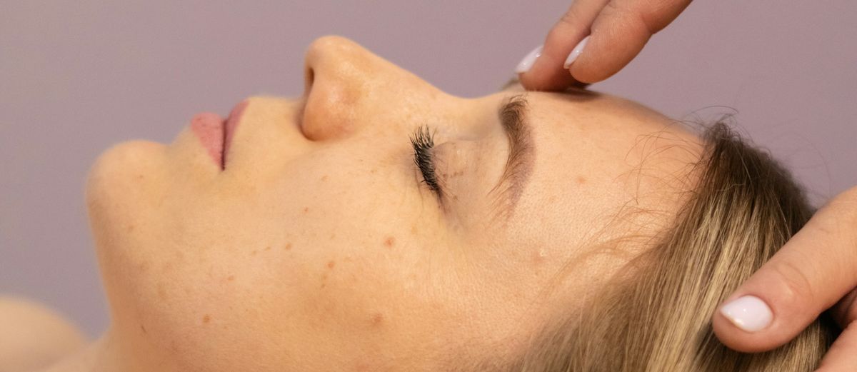 Fingertips resting at the brow of a face turned to one side, eyes closed.