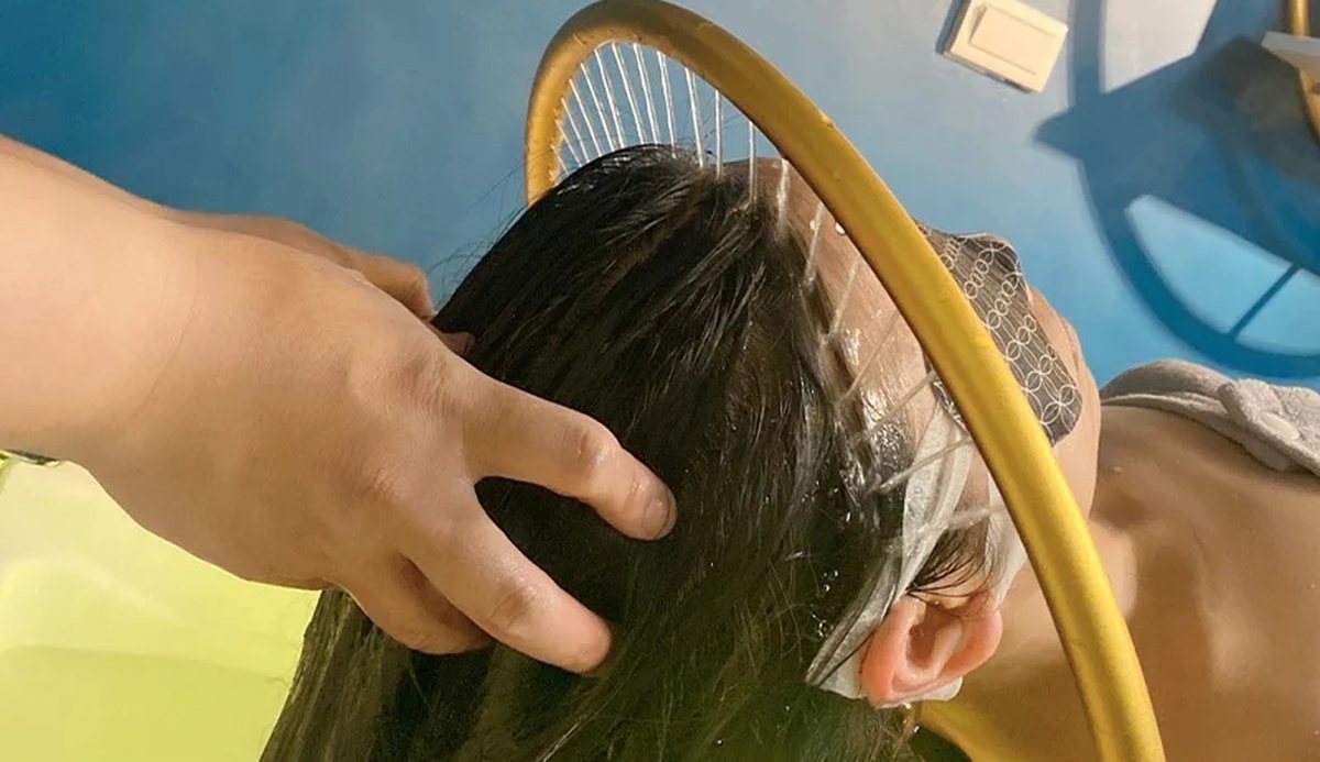 Warm water raining from a golden halo onto the scalp of someone lying at the basin, one hand working the hair.