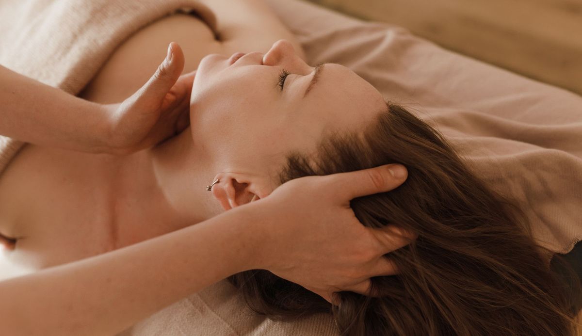Two hands cradling the head of someone lying down with their eyes closed.